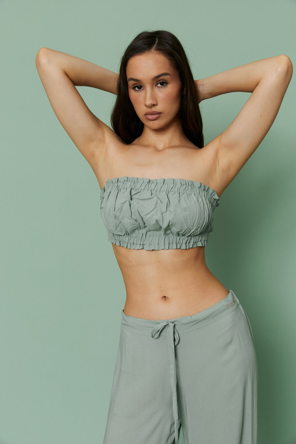 Model posing with hands behind head in Azalea Green Voile Crop top and pants, showcasing ruched texture and breathable strapless silhouette.