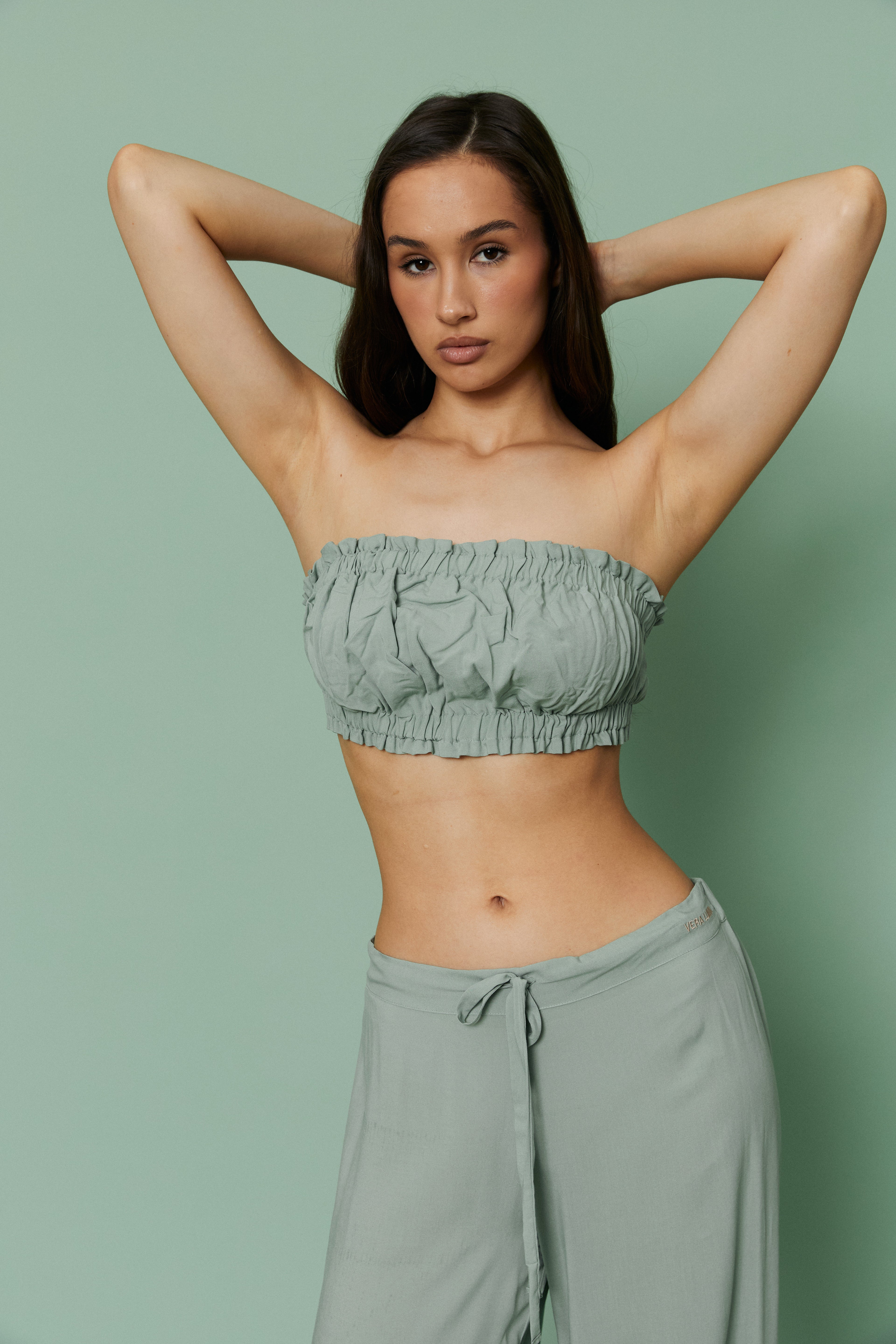 Model posing with hands behind head in Azalea Green Voile Crop top and pants, showcasing ruched texture and breathable strapless silhouette.
