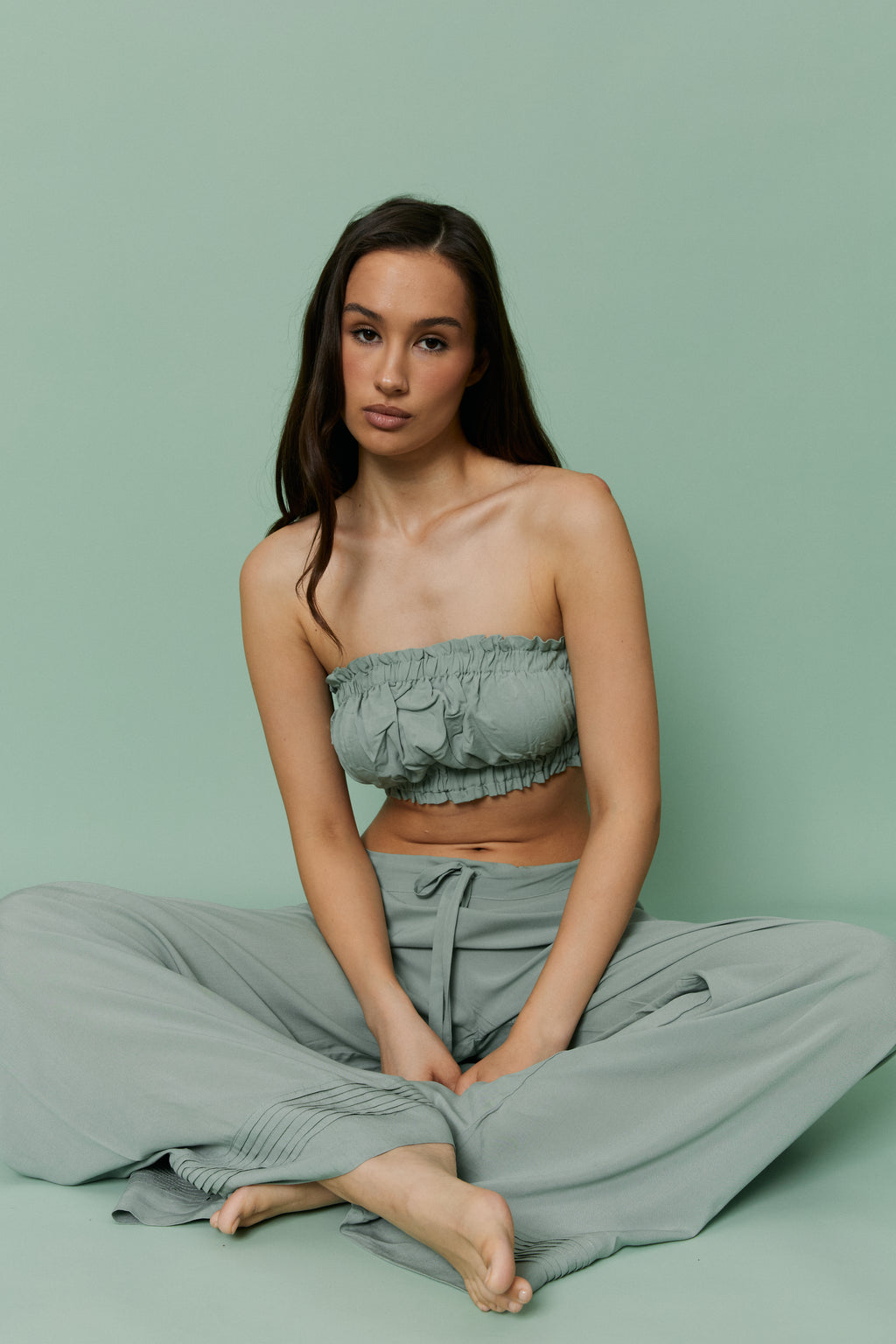 Seated model wearing Azalea Green Voile Lounge Bottom with matching ruched crop top, showcasing soft low-rise fit, lightweight sheer voile fabric and relaxed loungewear silhouette.