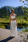 Full-length view of model standing on wooden deck by the lake wearing Azalea White Voile Lounge Bottom with matching crop top, showcasing soft flowing drape and relaxed luxury loungewear in natural sunlight.