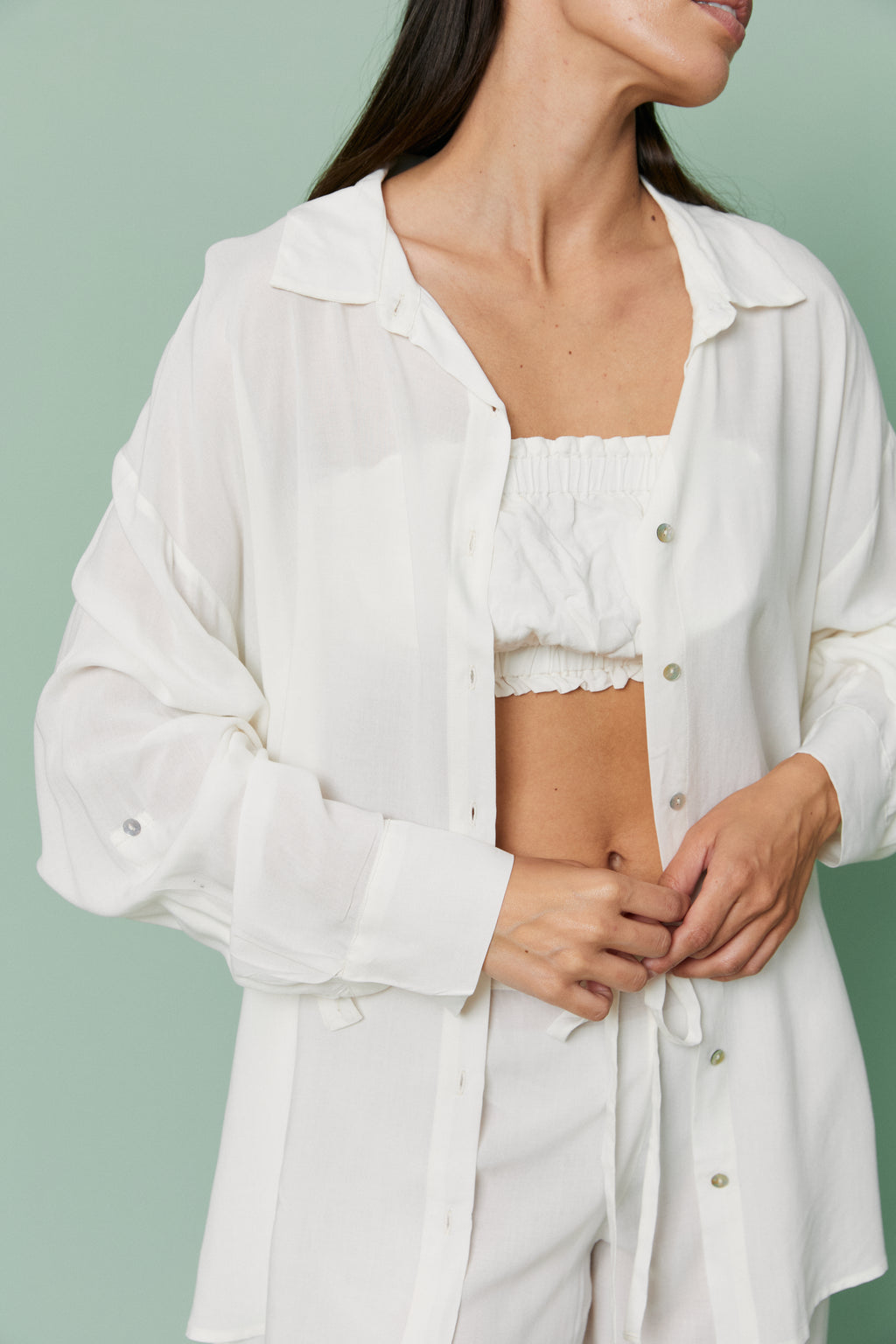 Model adjusting open Azalea White Voile Shirt over matching crop top, showcasing breathable fabric and relaxed button-front styling.
